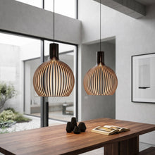 Cargar imagen en el visor de la galería, Two modern pendant lights hanging above a wooden table in a bright room with large windows.
