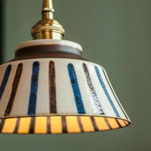 Load image into Gallery viewer, Striped lampshade with a gold fixture on a green background
