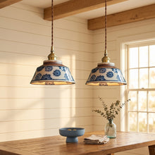 Load image into Gallery viewer, Two pendant lights with floral patterns hanging above a wooden table in a room with wooden beams and a window.
