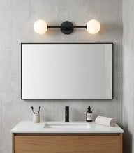 Load image into Gallery viewer, Bathroom vanity with mirror, light fixture, and toiletries against a gray wall.
