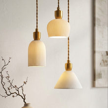 Load image into Gallery viewer, Three modern pendant lights with ribbed white shades and brushed gold metal accents, hanging at different heights against a light beige wall with decorative branches and a bowl.
