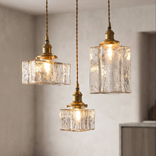 Load image into Gallery viewer, Three hanging pendant lights with clear textured glass shades and brass-toned metal fixtures, suspended in a softly lit interior room.
